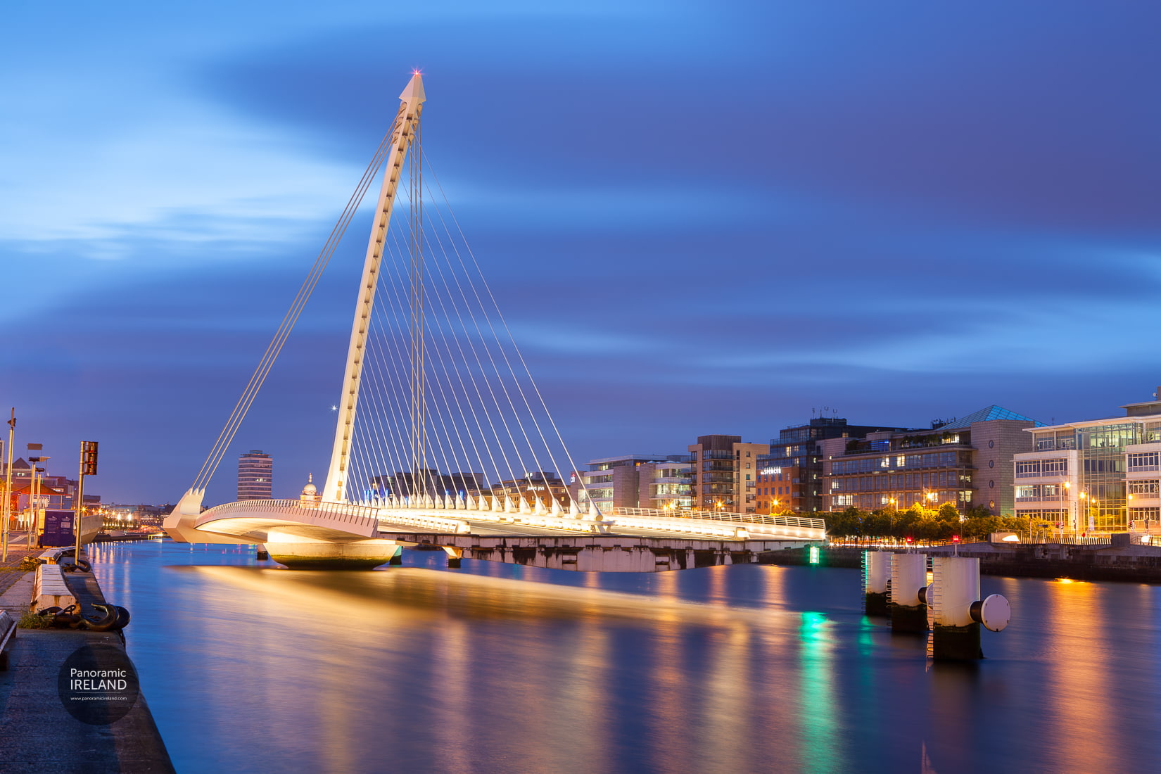 Dublin's Samuel Beckett Bridge at night, closed for maintenance, as the the city lights shine illuminating the cloudy sky and River Liffey.